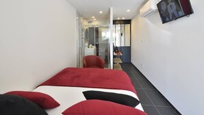 Une chambre d’hôtel avec un lit, une chaise rouge, un bureau et un téléviseur.