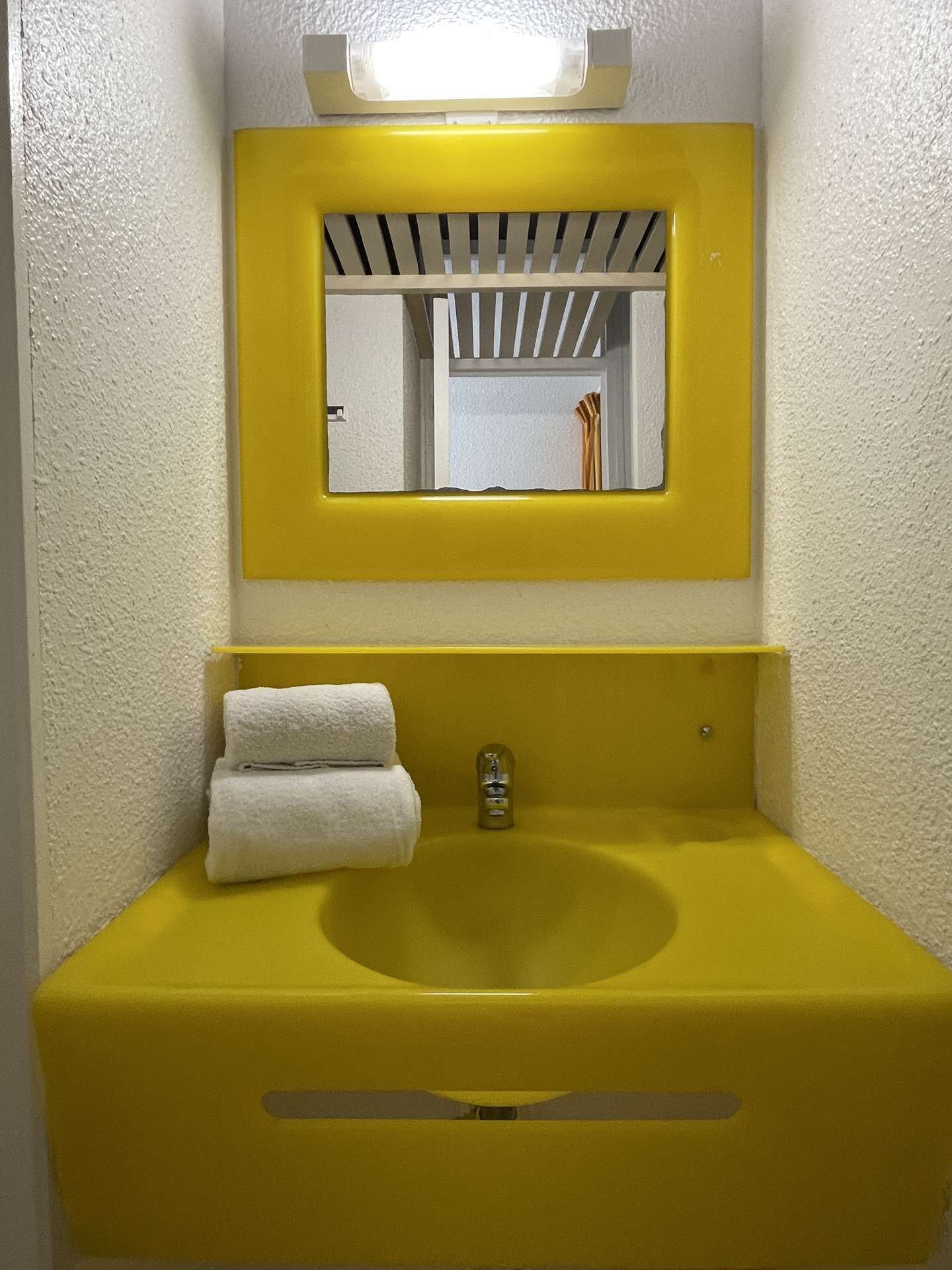 Une salle de bain avec un lavabo jaune, un miroir et deux serviettes.