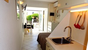 Une cuisine étroite avec un évier, un coin repas avec une table et des chaises, et une vue sur un jardin par une porte ouverte.