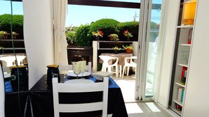 Un coin repas avec une table et des chaises, une bibliothèque et une vue sur un jardin, visible à travers des portes vitrées.