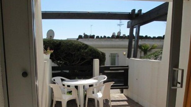 An outdoor patio with a table and chairs, a stone floor, and a view of a building with a green roof. - Port Nature Studio 22 - 2 people (AGDE)