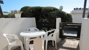 A patio with a white table and four white chairs, a black gate, and a hedge in the background. - Port Nature Studio 22 - 2 people (AGDE)