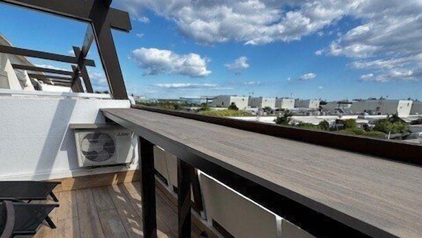 En tagterrasse med træterrasse, udendørs møbler og udsigt til omkringliggende bygninger.