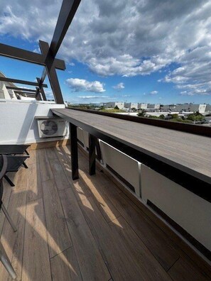 Een terras op het dak met een houten dek, tuinmeubels en uitzicht op omliggende gebouwen.