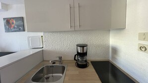 Eine Küche mit Spüle aus Edelstahl, einer schwarzen Kaffeemaschine und einer Mikrowelle.