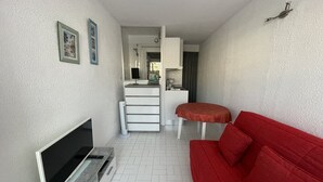 A compact living space with a flat-screen TV, a red sofa, a small dining table, and a kitchenette in the background. - Port Nature Studio 67 - 2 people (AGDE)