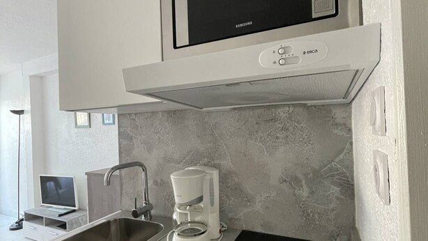 A modern kitchen with a built-in microwave, a coffee maker, a sink, and a black induction cooktop. - Port Nature Studio 67 - 2 people (AGDE)