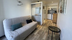 A modern living room with a sofa, a small table, and a kitchen area in the background. - Port Nature Studio 70 - 2 people (AGDE)