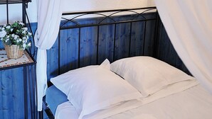 Un lit avec une literie blanche, une tête de lit en métal et une petite table sur laquelle se trouve un panier de fleurs.
