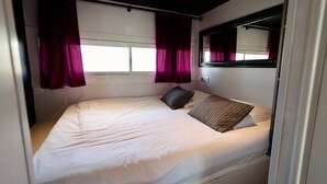 A single bed with a white mattress, two pillows, and a window with purple curtains. - DIAMANT - Port Nature Apartment 81 - Luxury - 2 people (AGDE)