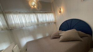 Makuuhuone, jossa on sänky, verhot, seinään kiinnitetty valaisin ja termostaatti.