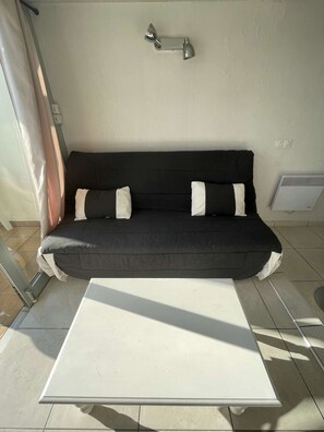 A black sofa with white cushions, a white table, and a wall-mounted light fixture. - Apartment Port Nature 87 - 2 people (AGDE)