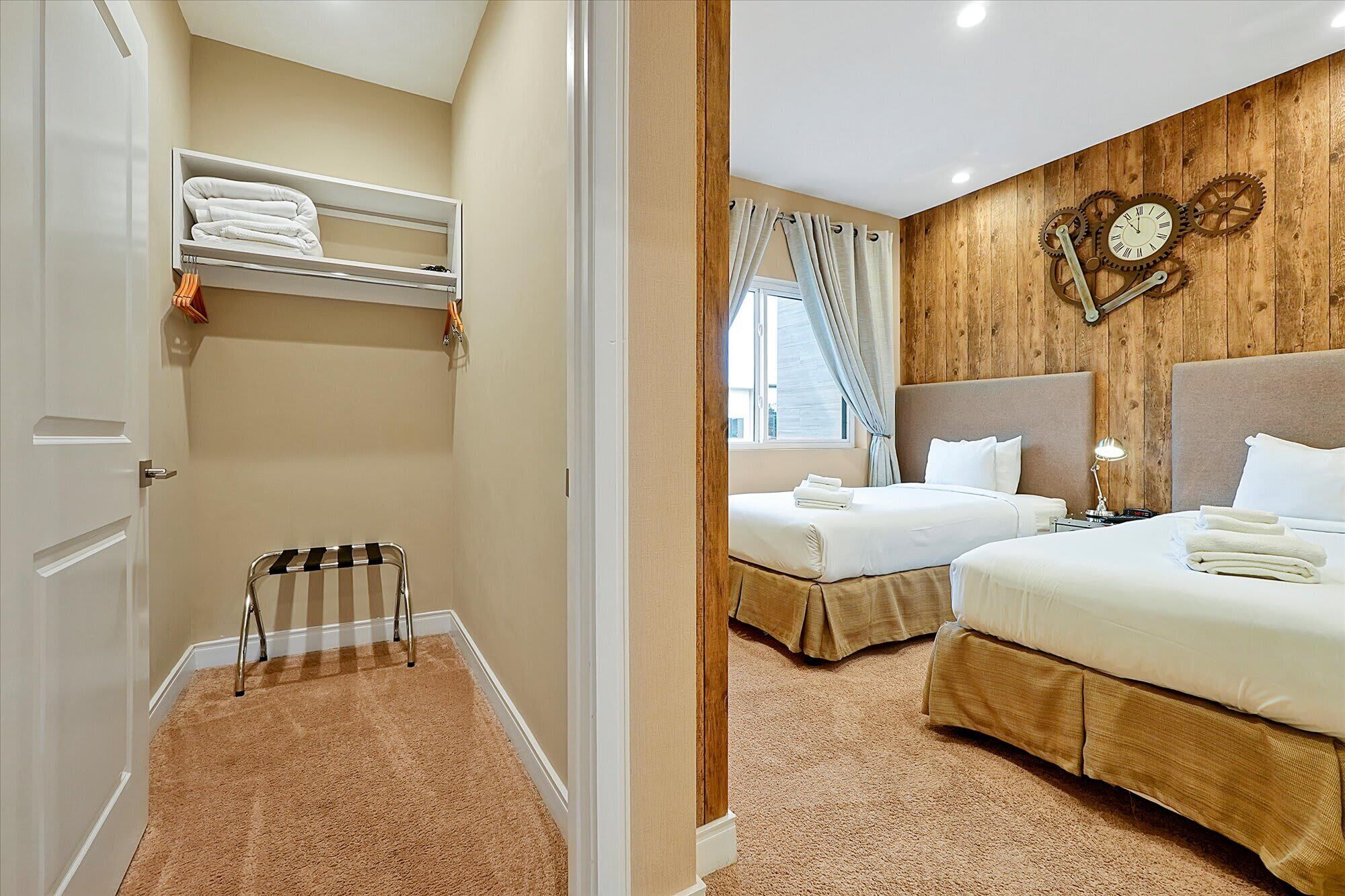 Habitación de hotel con dos camas, un reloj de pared de madera, una ventana con cortinas y un radiador pequeño.