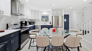 Une cuisine moderne dotée d’un îlot central, d’appareils électroménagers en acier inoxydable et d’un coin repas avec une table et des chaises en verre.