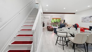 Un intérieur moderne avec un escalier, un coin repas doté de tabourets de bar et une vue sur la verdure à l’extérieur.