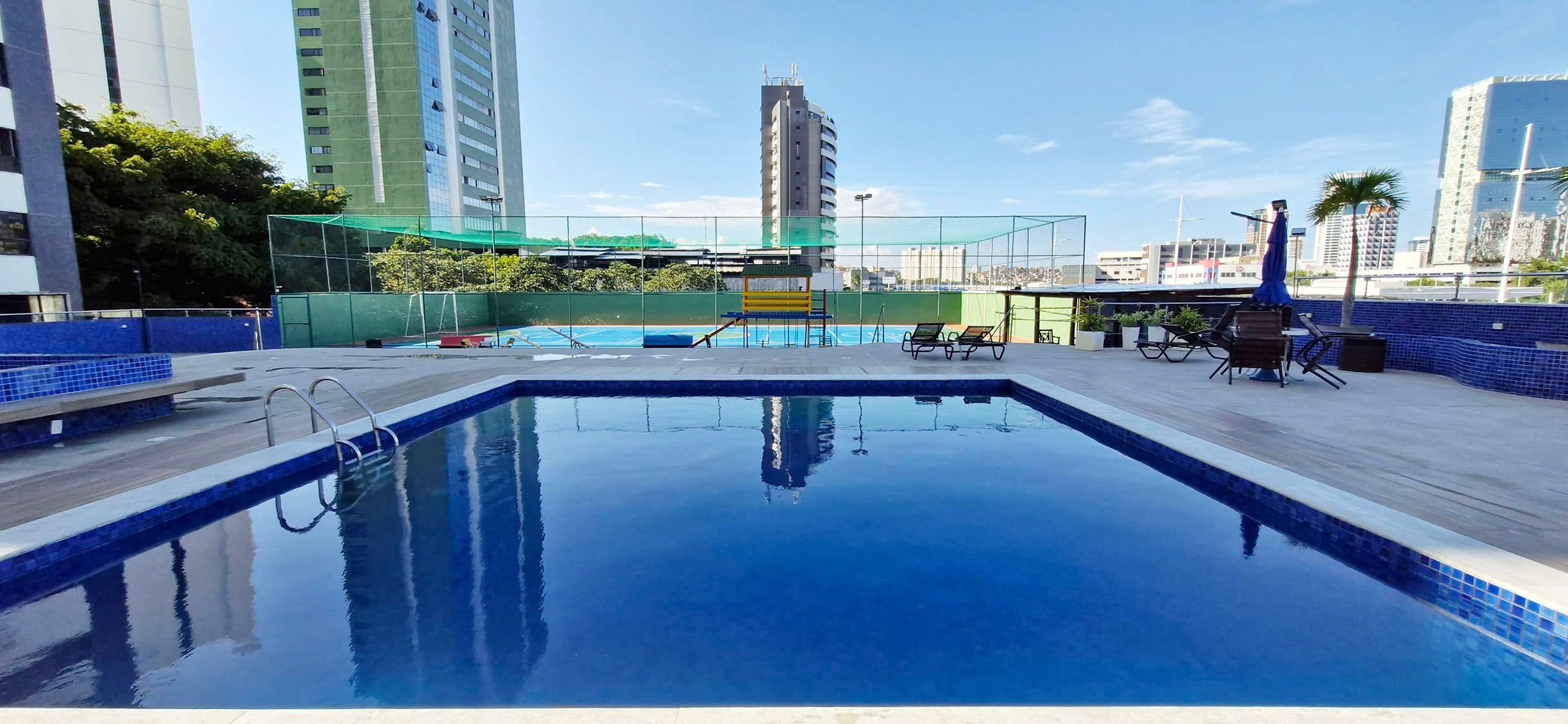 Una piscina en la azotea con vistas despejadas del horizonte urbano, incluyendo rascacielos y un campo deportivo al fondo.