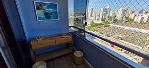 A balcony with a city view, a wooden bench, a woven basket, and a framed picture on the wall. - COPBV0101 - Edificio Torres do Iguatemi (Salvador)
