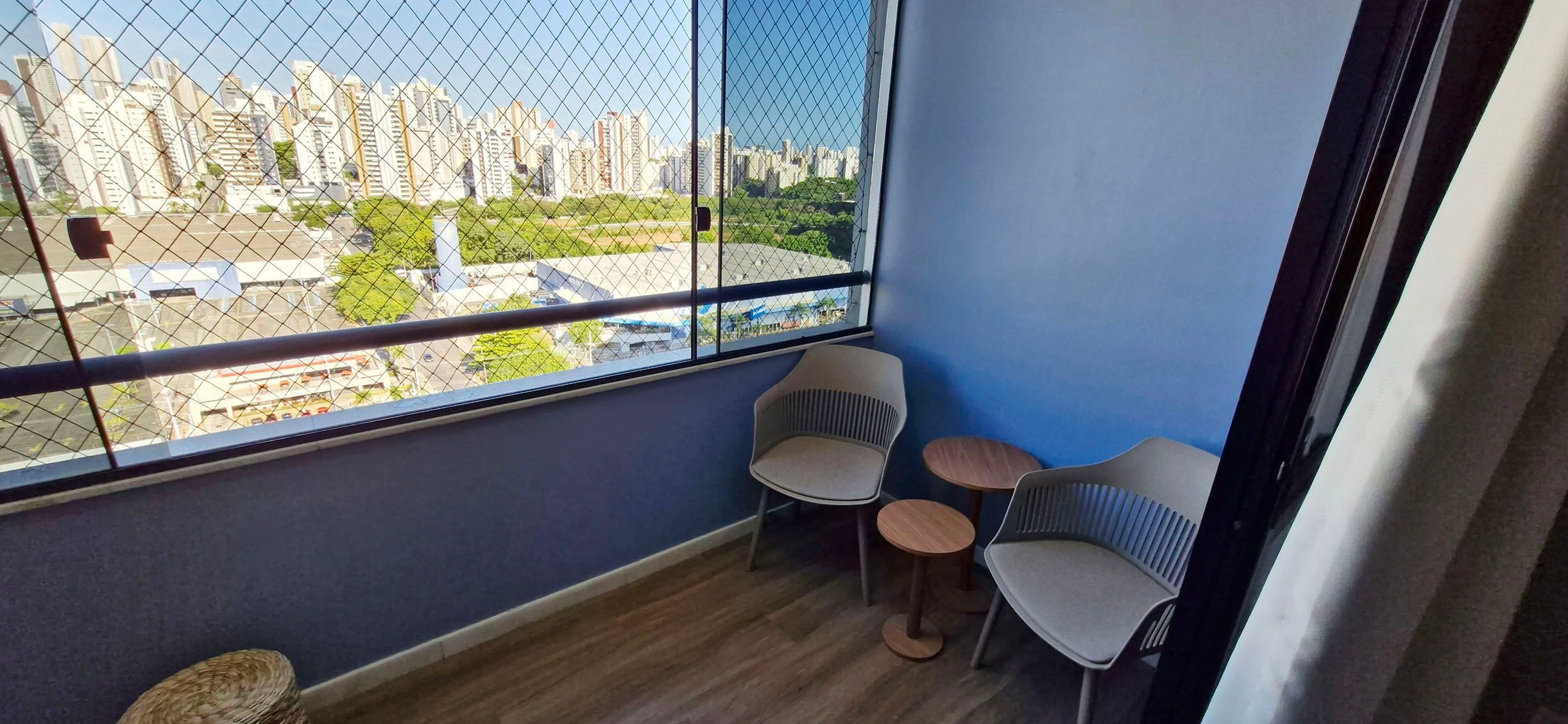 A balcony with a city view, two chairs, a small round table, and a woven stool.