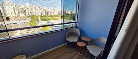 A balcony with a city view, two chairs, a small round table, and a woven stool.