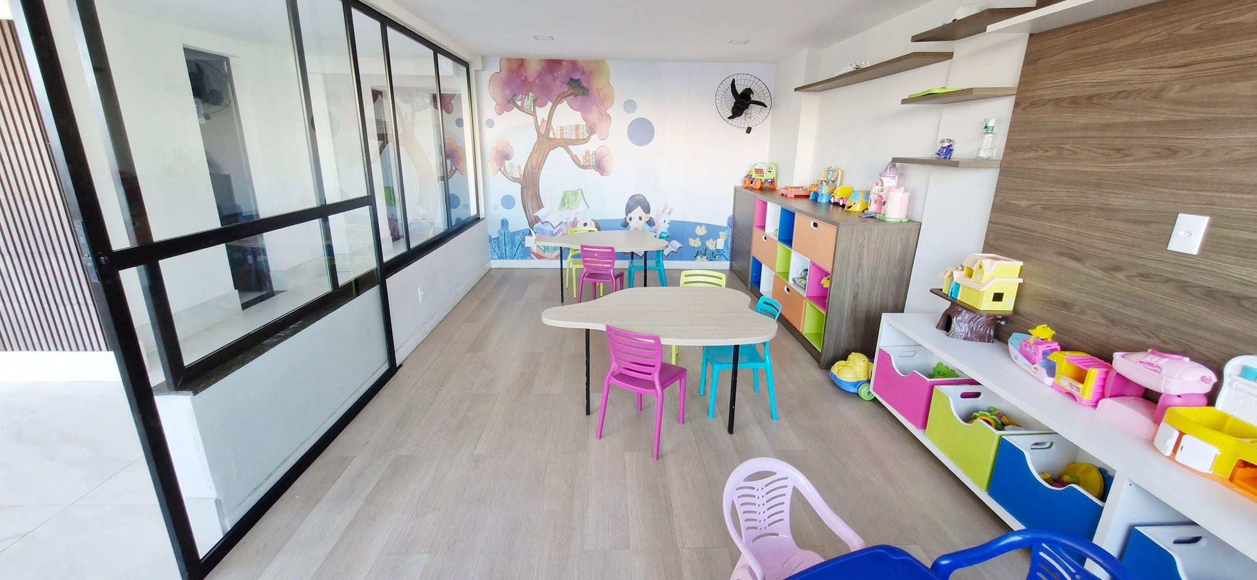 Un cuarto de juegos infantil con un ventanal grande, un mural y unidades de almacenamiento de colores.