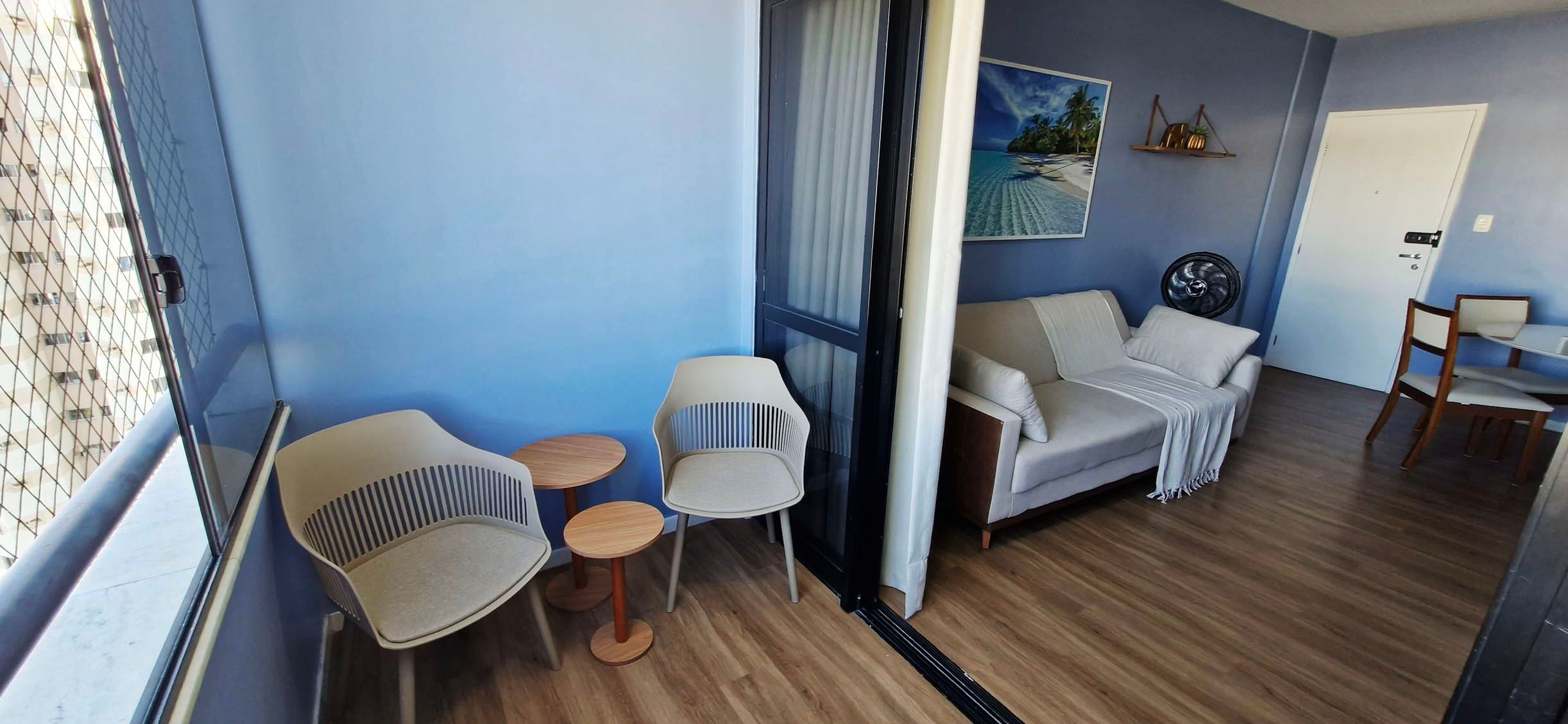 A room with a sofa, two chairs, a small table, a fan, and a door.