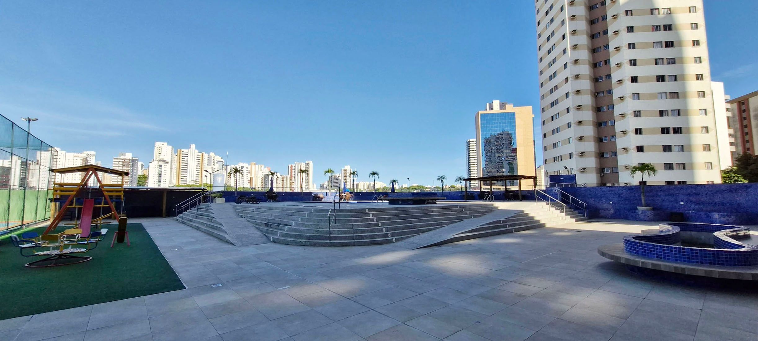 Terraza en la azotea con un parque infantil, una zona de estar circular y vistas de edificios altos circundantes.