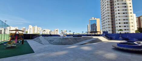 Terraza en la azotea con un parque infantil, una zona de estar circular y vistas de edificios altos circundantes.