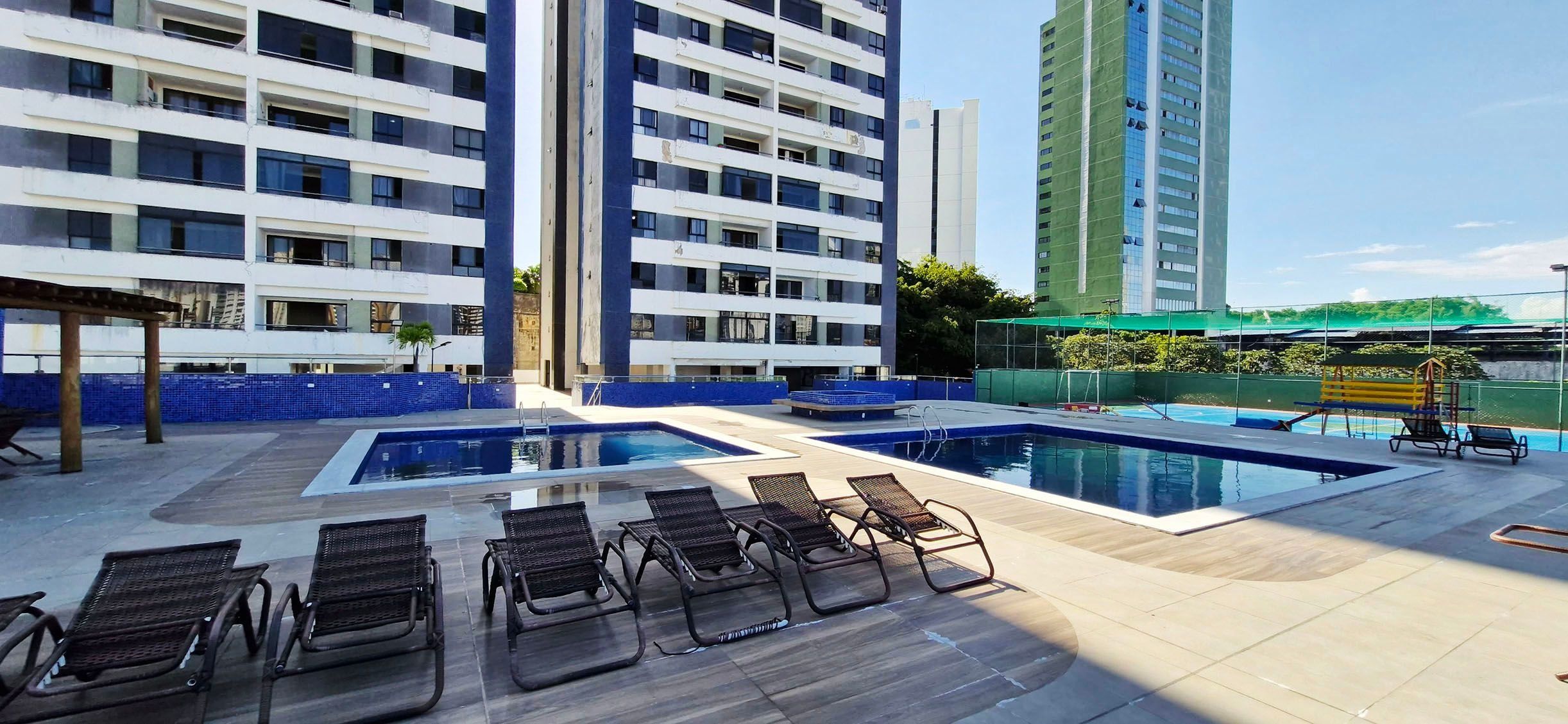 A rooftop pool area with multiple pools, lounge chairs, and high-rise buildings in the background.