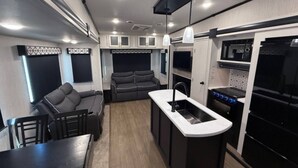 A compact RV interior with a kitchenette, seating area, and a dining table.