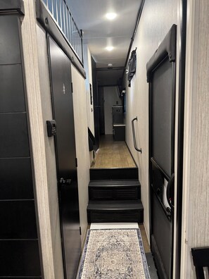 A narrow hallway with a wooden floor, a patterned rug, and a staircase leading to another room.