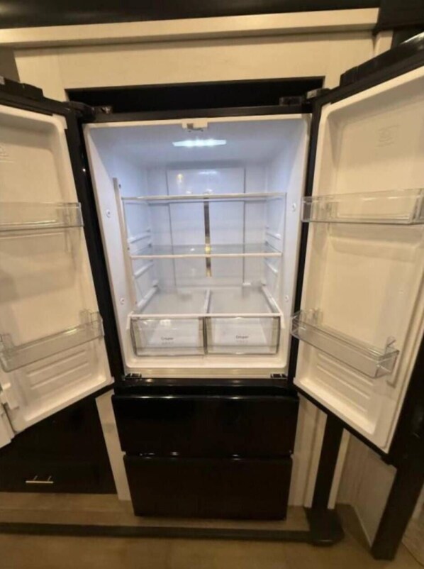 Un refrigerador negro con dos puertas abiertas, mostrando estantes y cajones vacíos.