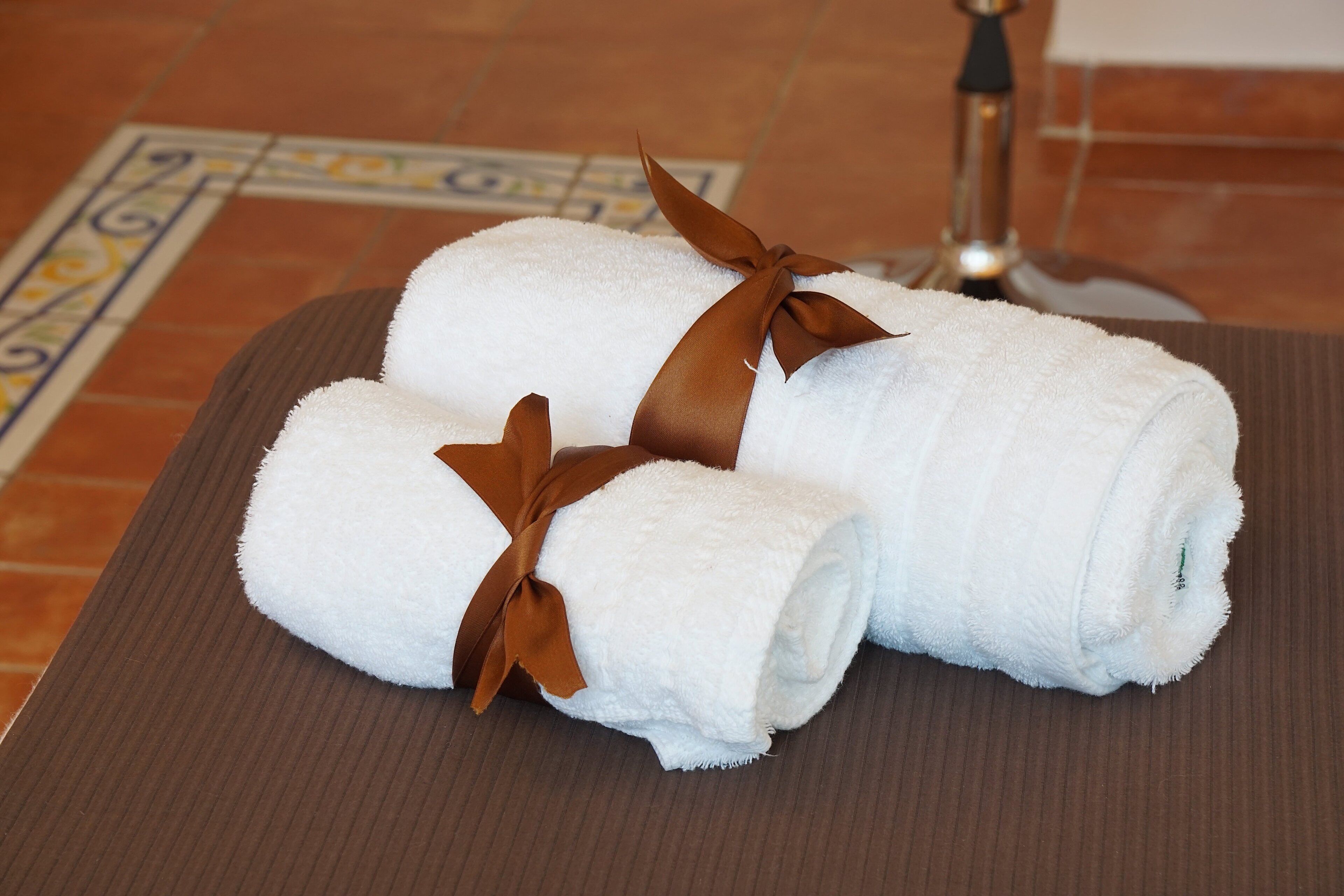 Three white towels with brown ribbons tied around them, placed on a brown tray.