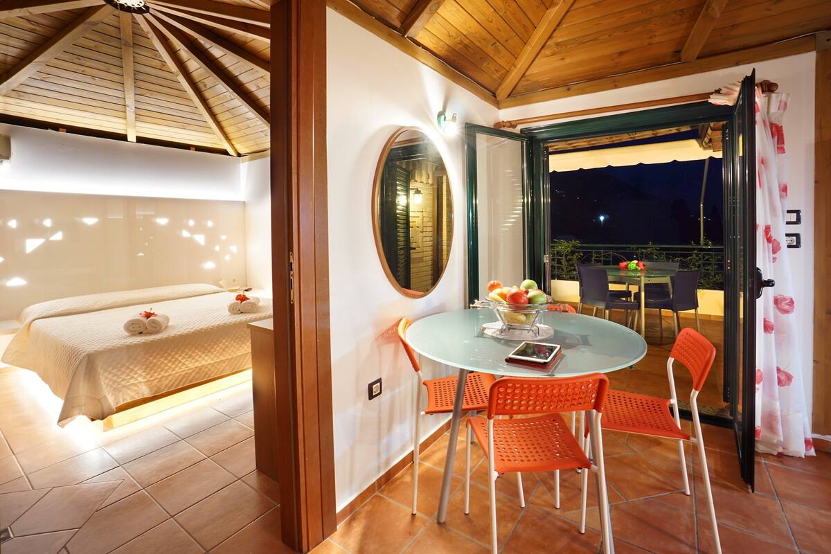 Egy hálószoba, amelyben található egy ágy, egy kerek tükör, valamint egy étkező, ahol egy asztal és székek állnak.