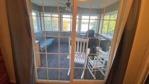 A room with a sliding glass door leading to an outdoor deck with a ceiling fan, a blue sofa, and a white railing. - Water Front Lake House - Black Lake, NY (Ogdensburg)