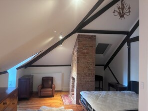 A bedroom with a sloped ceiling, a brick fireplace, a wooden chair, a bed, and a dresser.