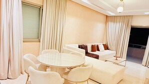 Ein modernes Wohnzimmer mit einem runden Esstisch, weißen Sofas und einem großen Fenster mit Vorhängen.