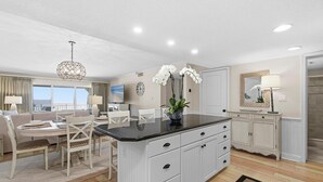 A modern kitchen with a central island, white cabinetry, and a dining area with a table and chairs. - Sandpiper 514 (New Smyrna Beach)