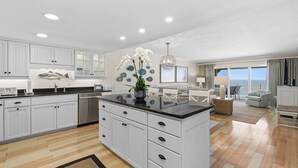 A spacious kitchen with white cabinetry, a central island, and a view to the living area. - Sandpiper 514 (New Smyrna Beach)