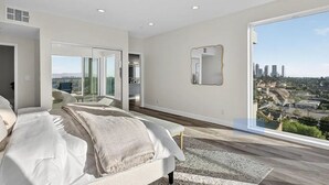 Een moderne slaapkamer met een groot bed, een inloopkast, een badkamer en uitzicht op de stad.
