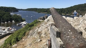Um grande canhão numa elevação rochosa com vista para uma marina com barcos.