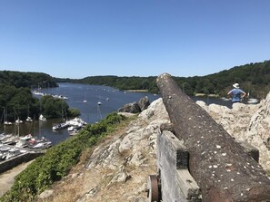 Een groot kanon op een rotsachtige richel met uitzicht op een jachthaven met boten.