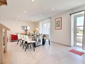 Een moderne eetruimte met een centrale tafel, stoelen en een spiegel aan de muur.
