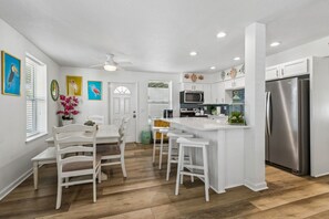 A modern kitchen with white cabinetry, a stainless steel refrigerator, and a dining area with white chairs. - Updated 6-bedroom, 4 bath cottage across from the beach with a private pool (Fernandina Beach)