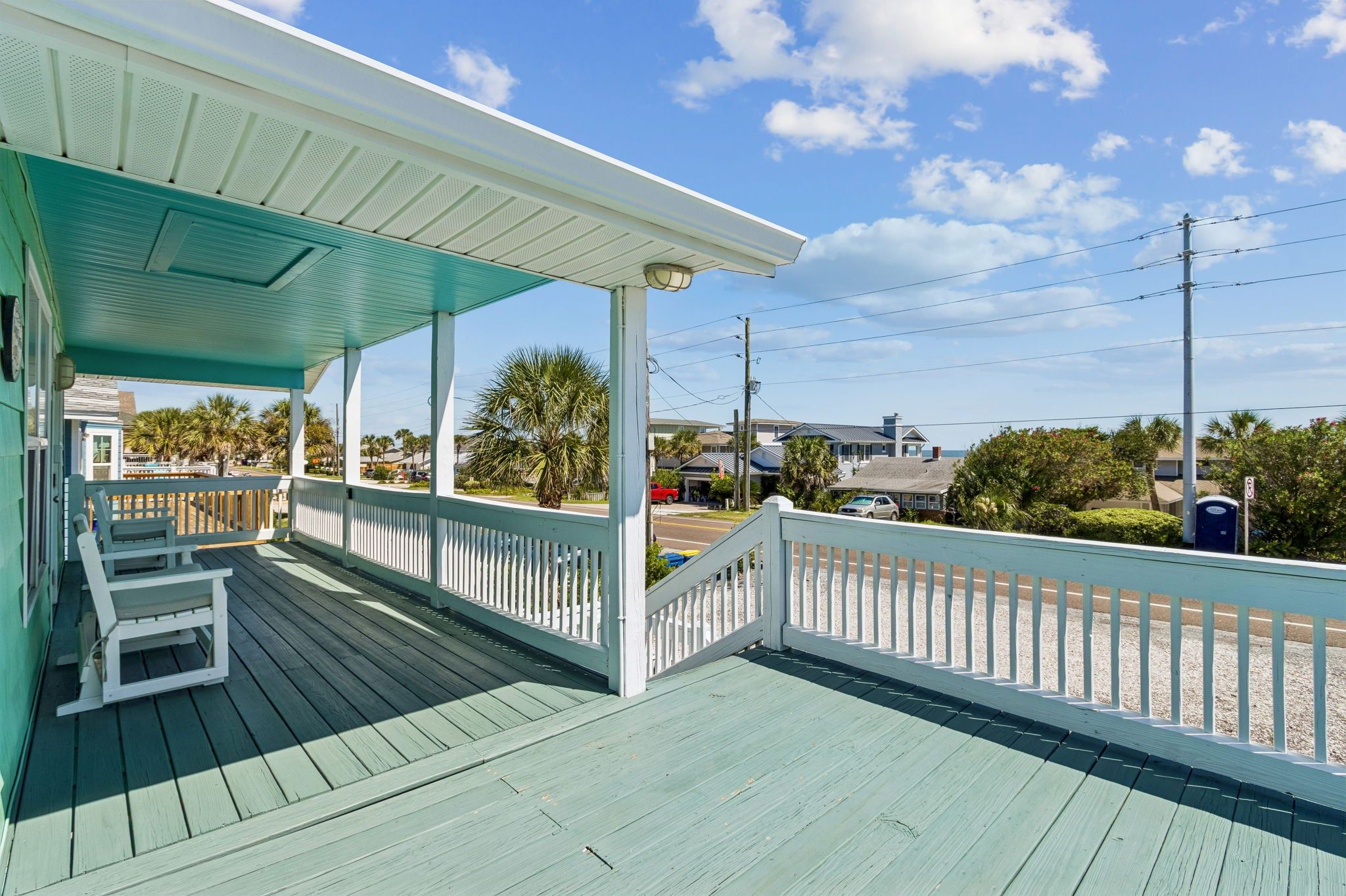 A covered porch with a view of the beach and ocean, wooden deck, and a railing.