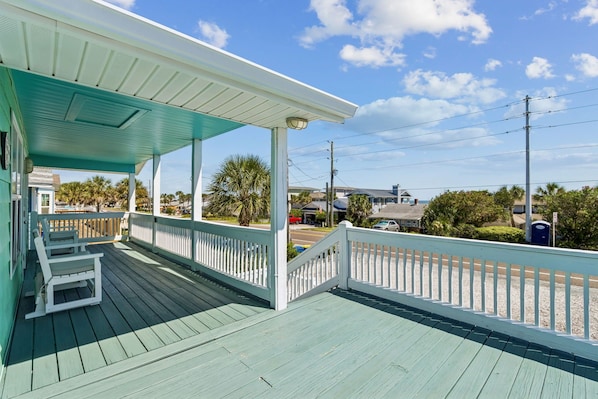 Eine überdachte Veranda mit Blick auf Strand und Meer, eine Holzterrasse und ein Geländer.