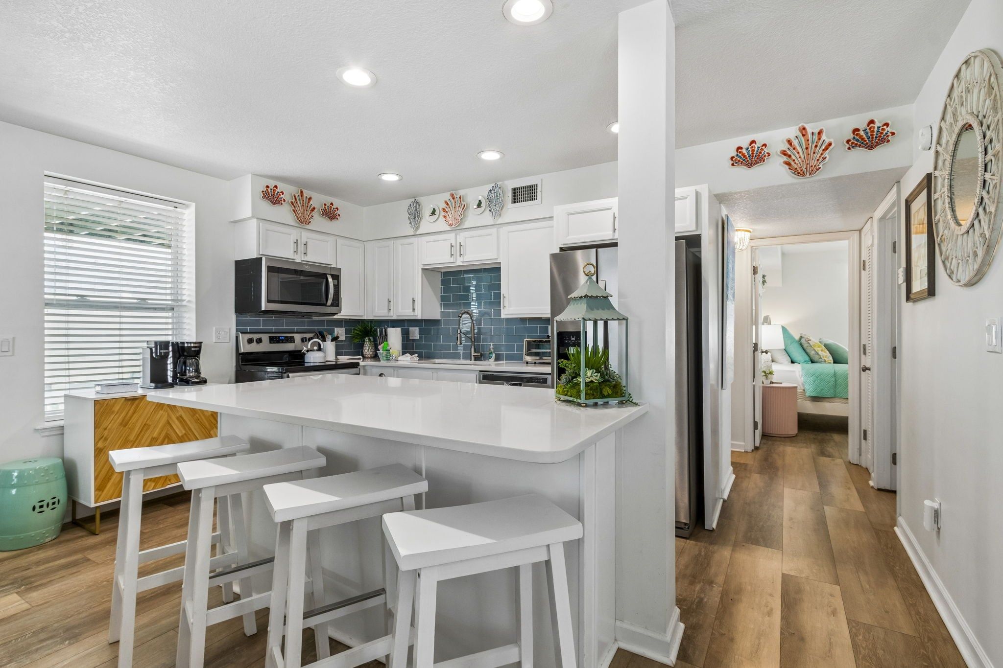 Una cocina moderna con muebles blancos, una isla central con taburetes altos, microondas y refrigerador.