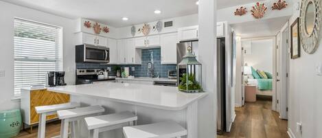 A modern kitchen with white cabinetry, a central island with bar stools, a microwave, and a refrigerator.