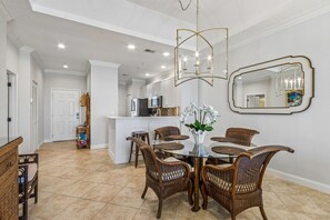 A dining area with wicker chairs and a glass table, a kitchen with white cabinets, and a large mirror on the wall. - Oceanfront Penthouse Retreat – 7th Floor at Ocean Place (Fernandina Beach)