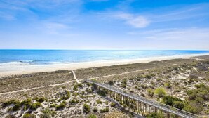 Ein Strand mit einer hölzernen Prominade, die zum Wasser führt, Sanddünen und einem klaren Himmel.