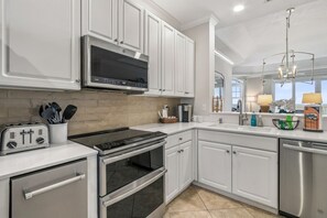 A modern kitchen with stainless steel appliances, white cabinetry, and a large window providing natural light. - Oceanfront Penthouse Retreat – 7th Floor at Ocean Place (Fernandina Beach)